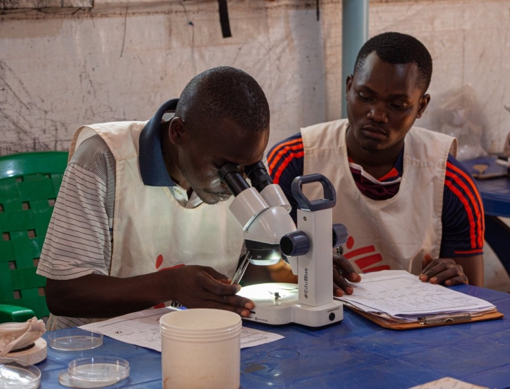 Julien Riyazimana y Paul Tuyininahaze, técnicos de control de vector, examinan mosquitos con el microscopio que han sido atrapados por las trampas puestas en las casas de diferentes partes del campo de personas refugiadas de Nduta.